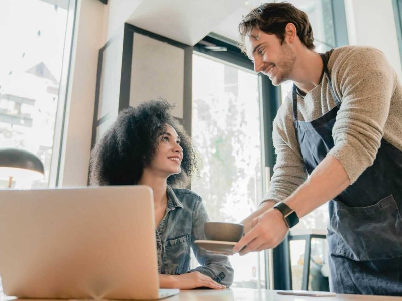 young-handsome-waiter-servicing-black-girl-customer-with-laptop-in-cafe.jpg